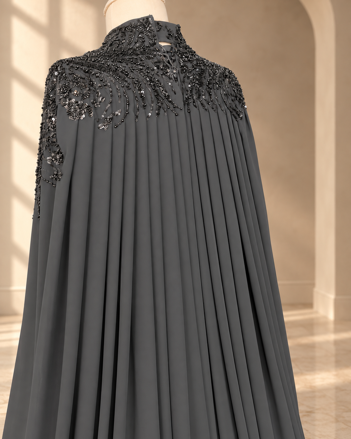 Back of the Selma charcoal gown: beaded shoulders and collar, with the cape falling in deep pleats