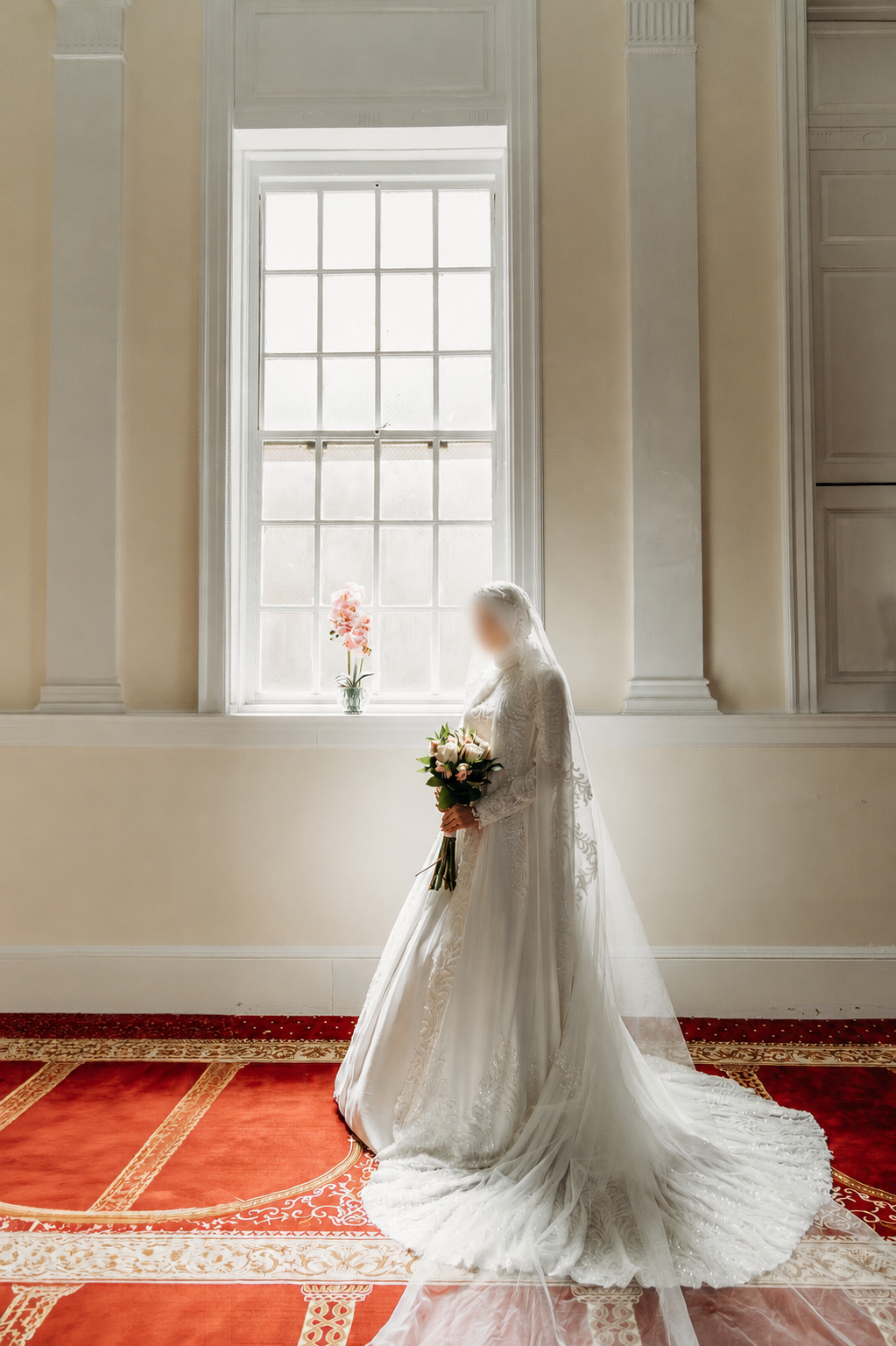 Person in a white wedding dress holding a bouquet in a room with red carpet and large window.