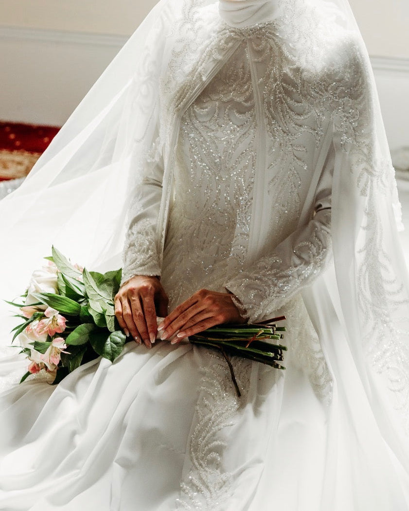 Person wearing a white wedding dress holding a bouquet indoors.