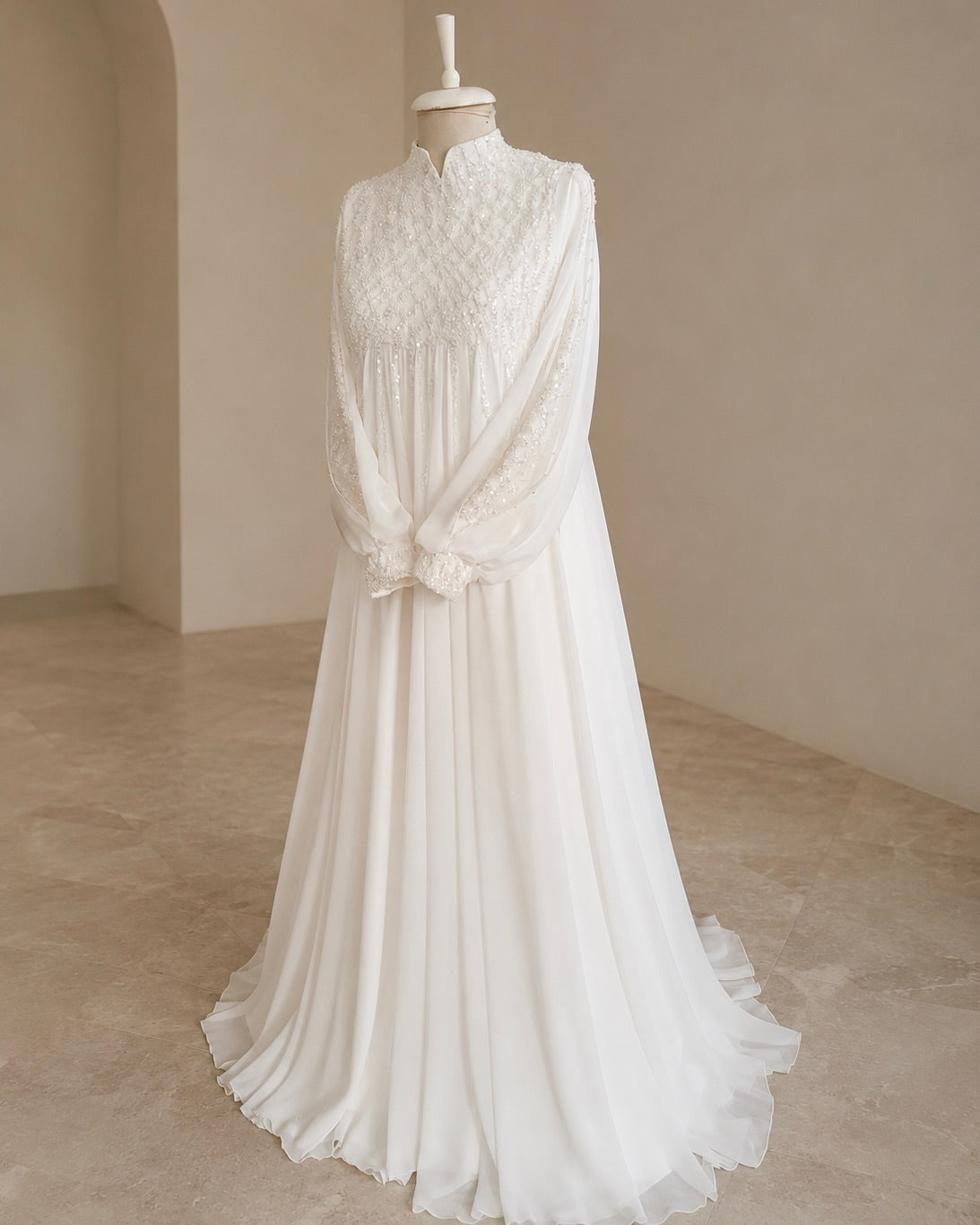 A white long-sleeve maxi dress with a textured embroidered bodice, high collar, and flowing chiffon skirt, displayed on a mannequin in a neutral indoor setting.